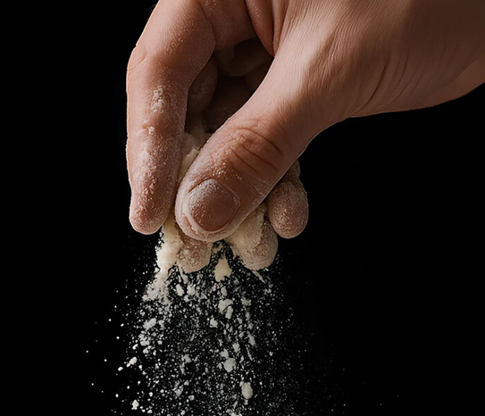 Mano soltando harina en suspensión sobre fondo negro, representando el riesgo de polvo fino en la industria alimentaria