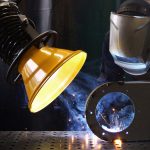 Brazo articulado de aspiración industrial con campana captando humos de soldadura en el punto de emisión.